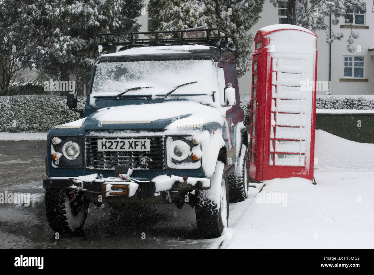 Due icone britannico coperto di neve bianca - Land Rover Defender 90 parcheggiato a fianco di un rosso inglese casella telefono su un inverno nevoso giorno - Ilkley, Inghilterra, Regno Unito. Foto Stock