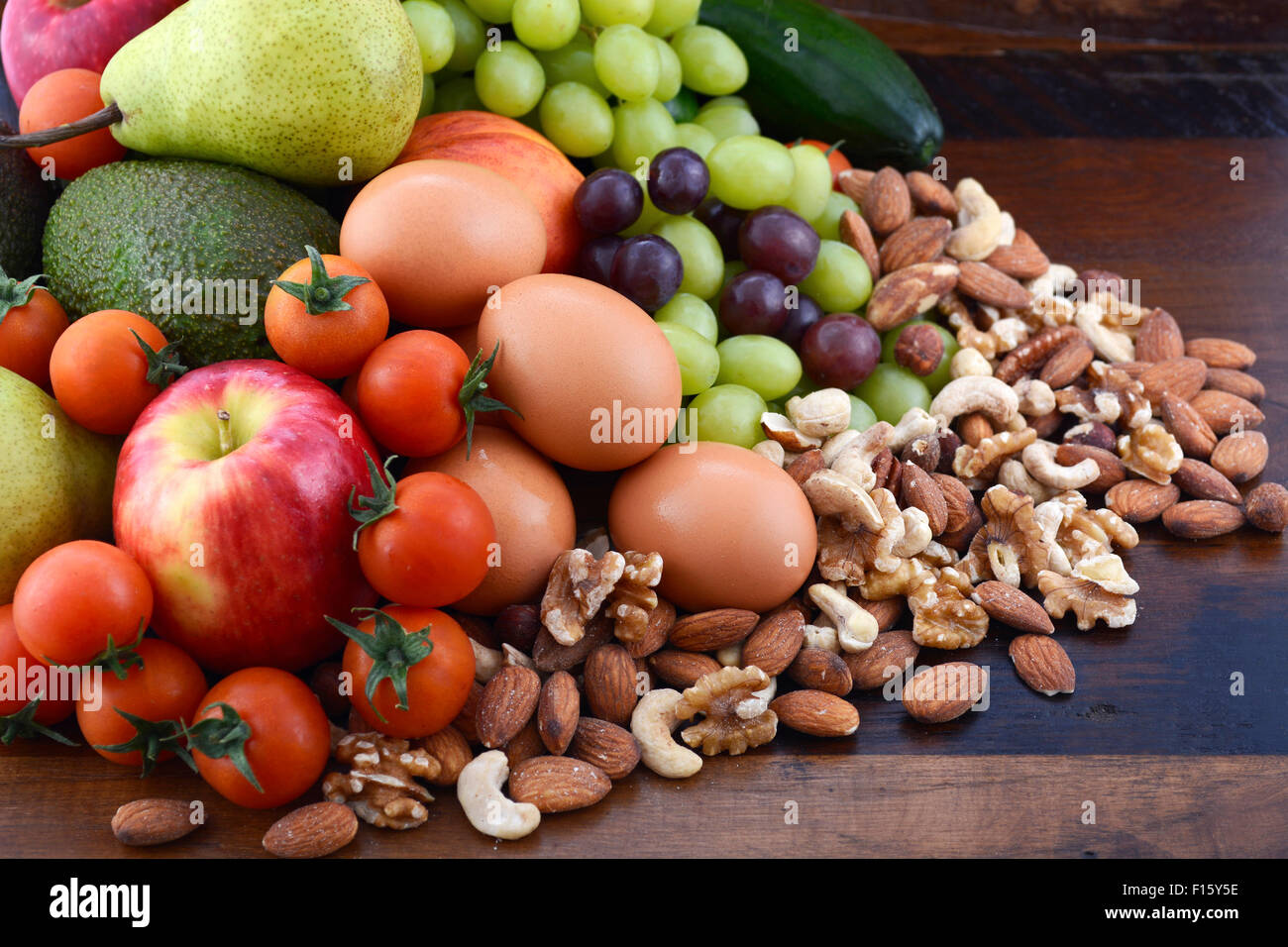 Alimentazione sana con frutta fresca, mele, pere, avocadi, uva, uova, frutta secca, pomodori cetrioli su un legno rustico sfondo. Foto Stock