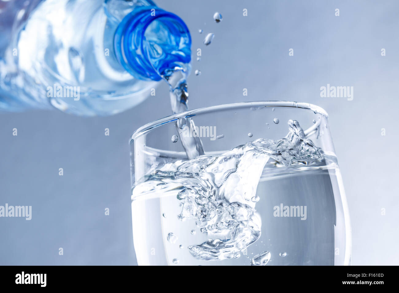 Versando acqua dalla bottiglia in vetro in tonificante blu Foto Stock