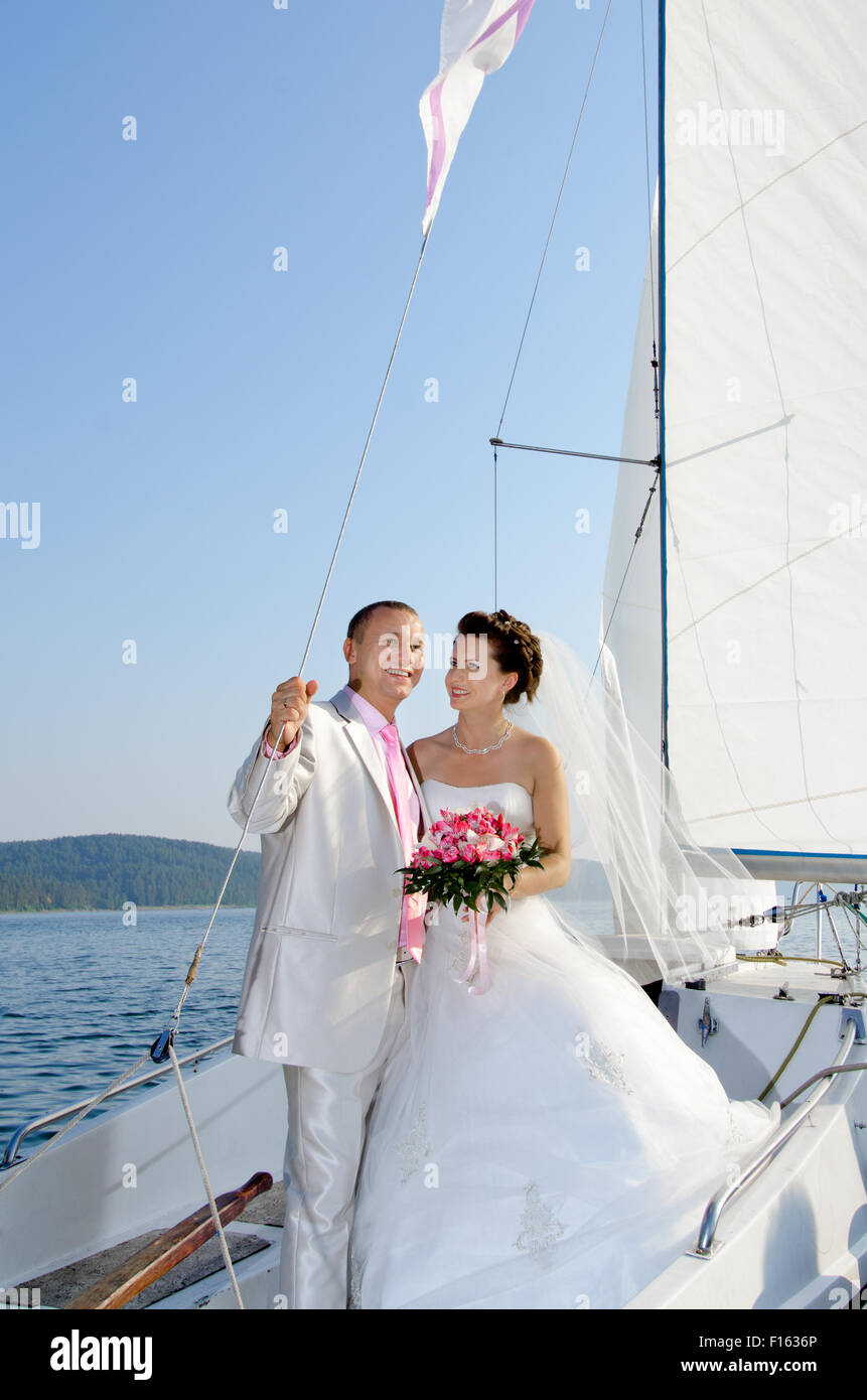 Foto verticale happy sposi stand su bianco yacht, all'aperto, viaggio di nozze Foto Stock
