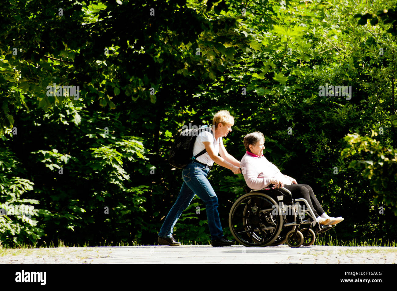 Donna spingendo un anziano donna disabile in carrozzella Foto Stock