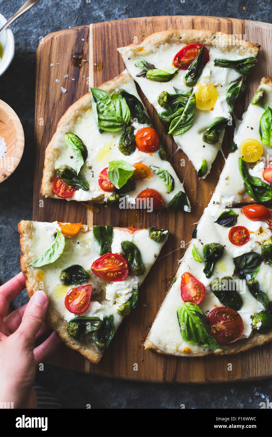 Padron di pepe e pomodoro ciliegino pizza, privi di glutine e grani. Una mano prendendo una fetta. Foto Stock