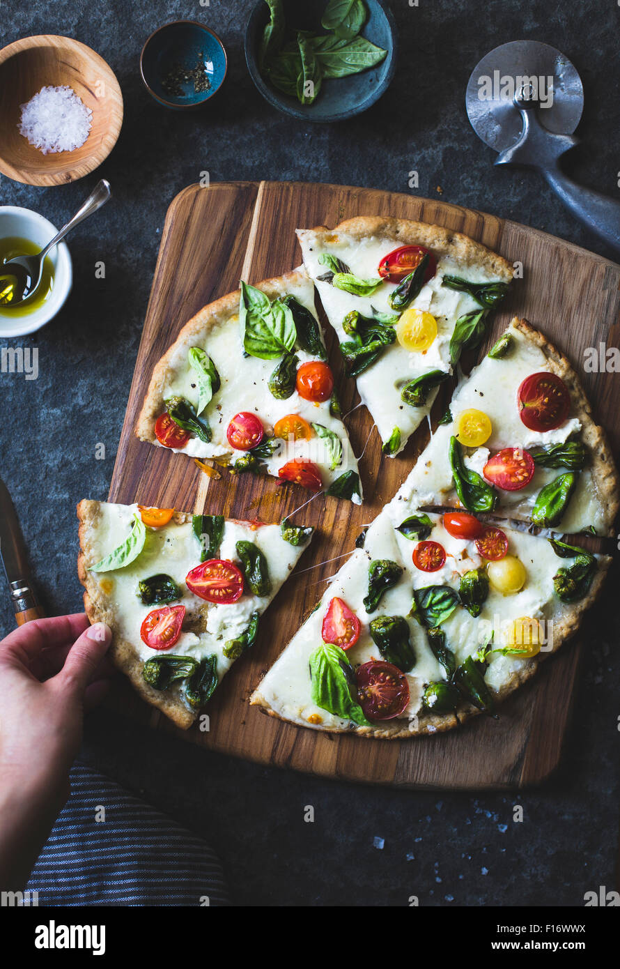 Padron di pepe e pomodoro ciliegino pizza, privi di glutine e grani. Una mano prendendo una fetta. Foto Stock