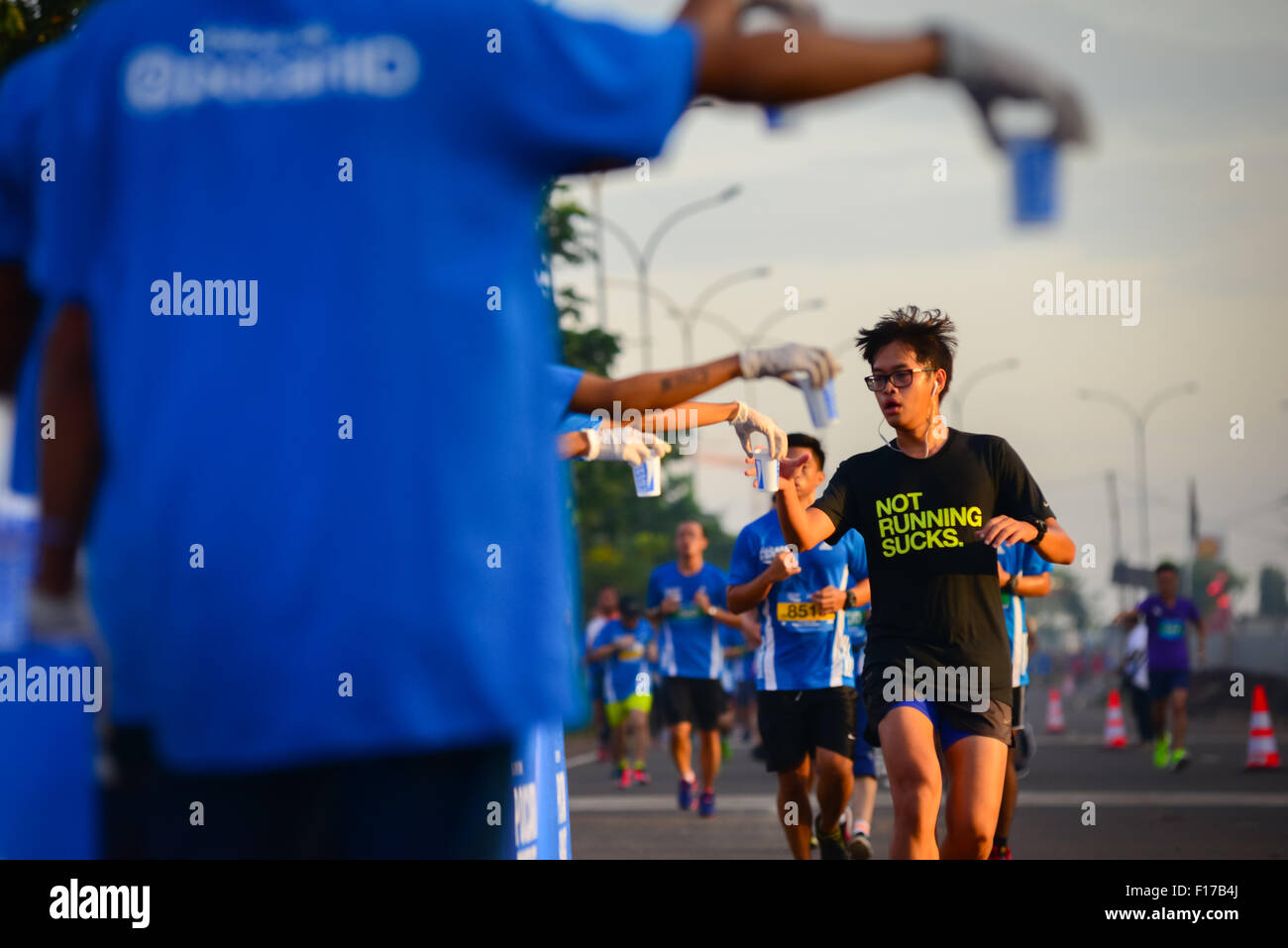 I corridori passano davanti a una stazione di bevande rinfrescanti mentre corrono nella corsa 'Pocari Sweat Run Indonesia 2015' a Tangerang, Indonesia. Foto Stock