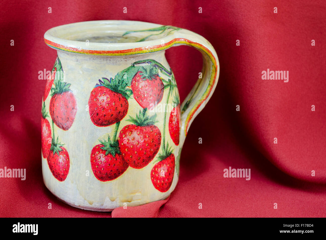 Decoupage decorate argilla modello fragola brocca sulla stoffa rossa sullo sfondo Foto Stock
