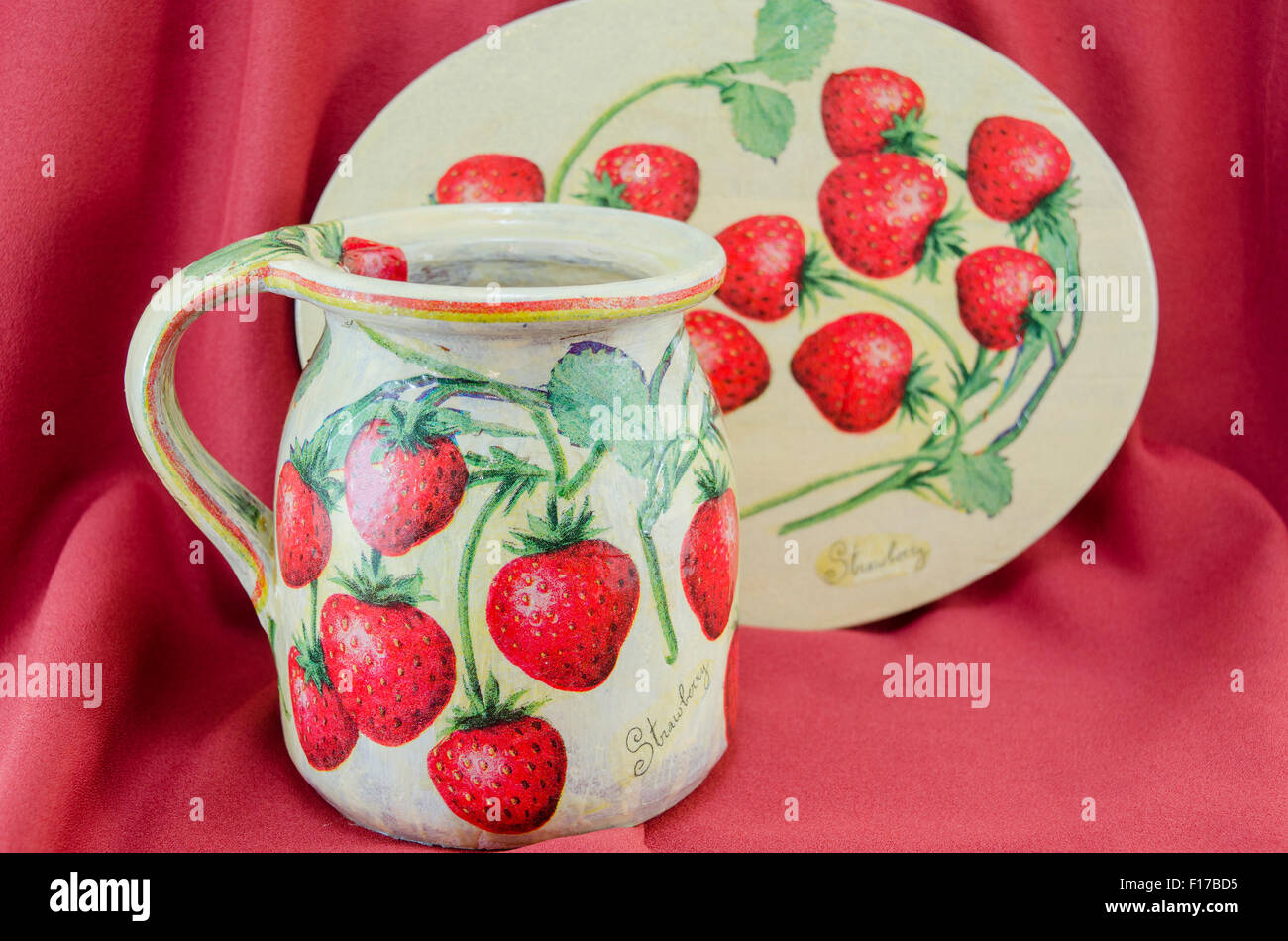 Decoupage decorate fragola modello brocca di argilla e la piastra sul tessuto rosso sfondo Foto Stock