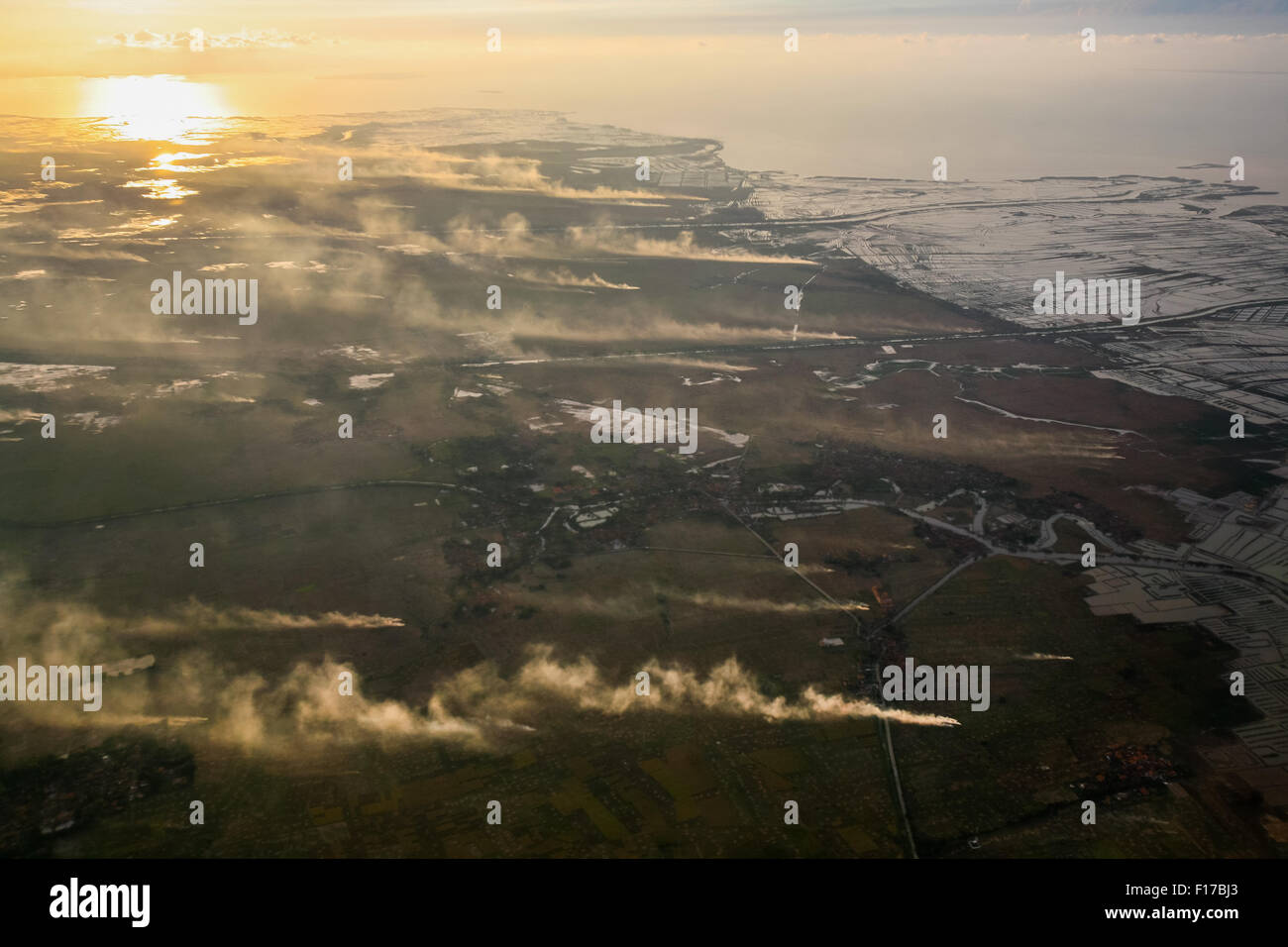 Vista aerea del paesaggio costiero che mostra campi agricoli, fumo, canali, allevamenti di gamberi marini e stagni di evaporazione del sale a Banten, Indonesia. Foto Stock