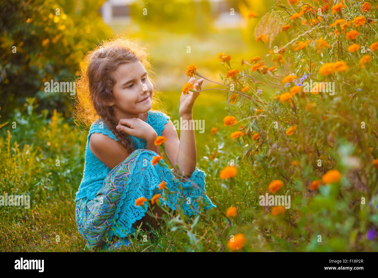 Teen ragazza seduta sul suo haunches e toccando fiore di arancia in Foto Stock