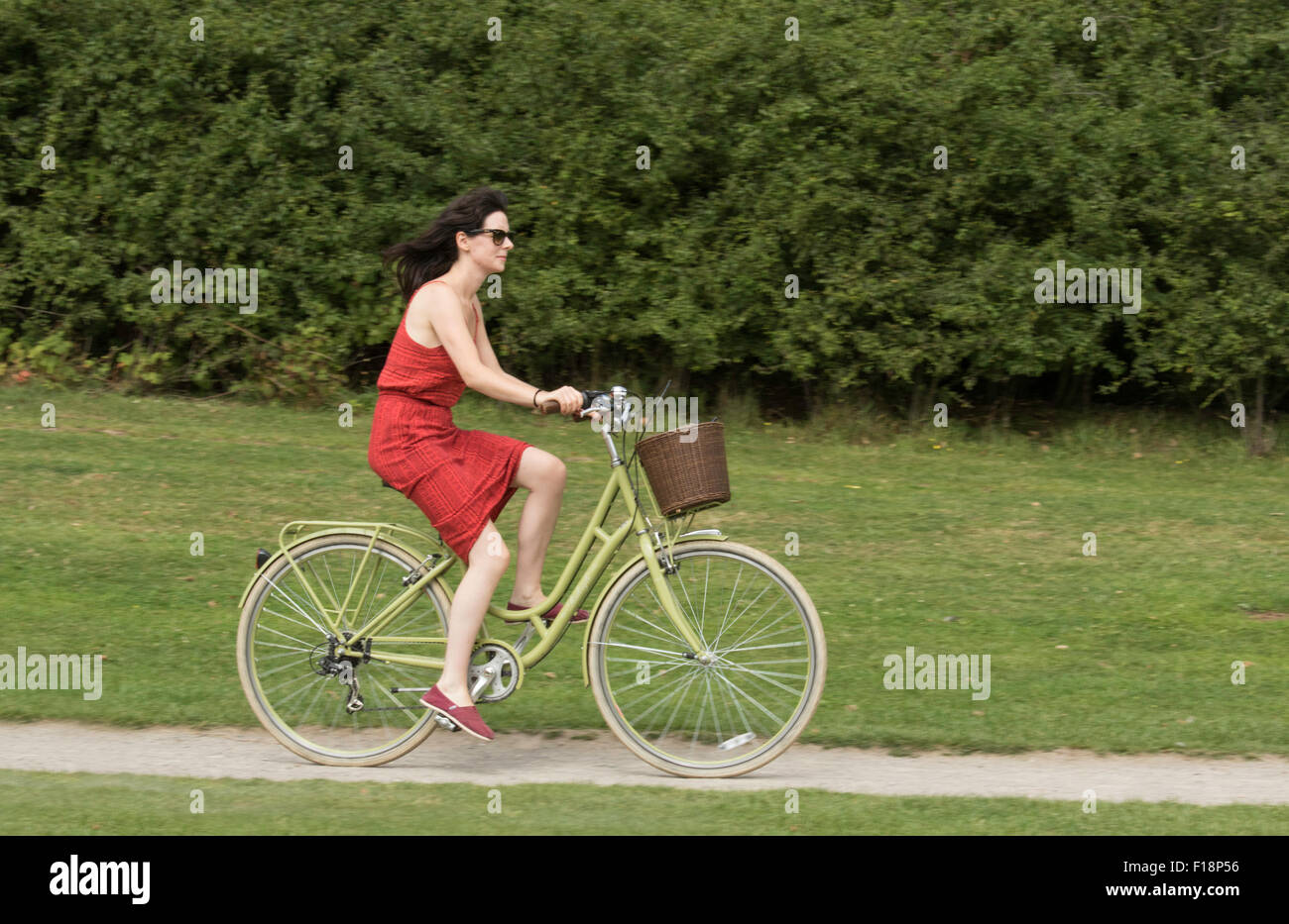 Signora in un abito rosso in bicicletta su una pista ciclabile, England, Regno Unito Foto Stock