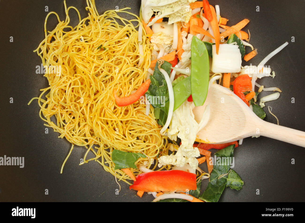 Primo piano di friggere ortaggi e Singapore tagliatelle con un cucchiaio di legno in un wok Foto Stock