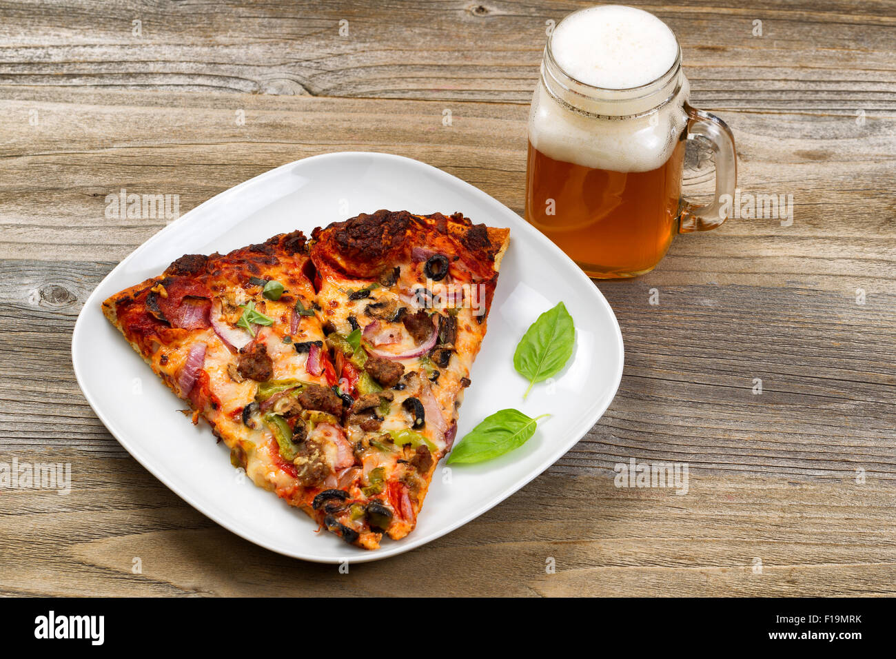 Due fette di pane appena sfornato la pizza in una piastra bianca con una pinta di giustamente si versa la birra impostazione su una tavola in legno rustico. Foto Stock