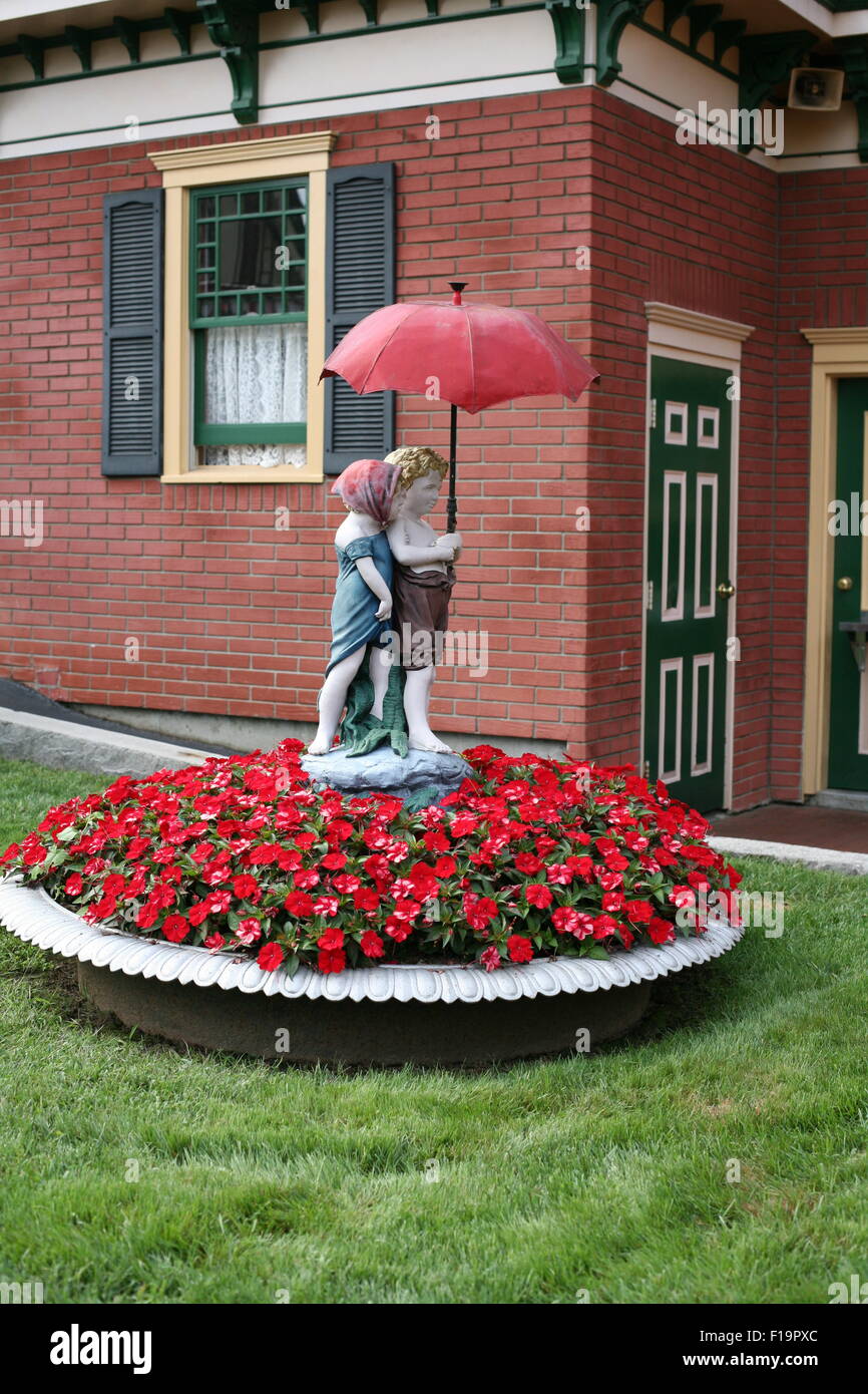 Statua di un ragazzo e una ragazza con ombrello sopra le loro teste,in  piedi in un letto di fiori rossi, New Hampshire, Clarks trading post Foto  stock - Alamy