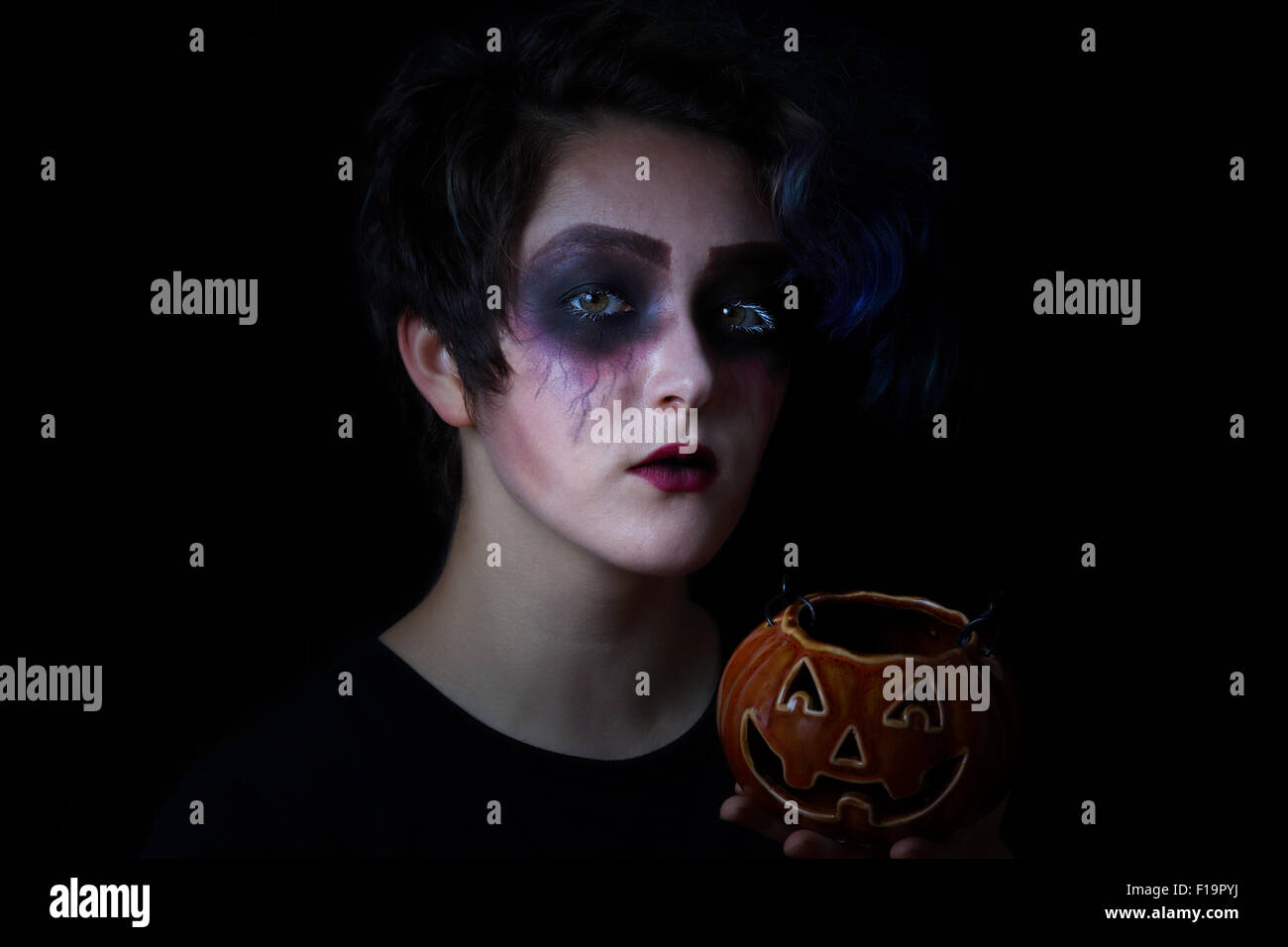 Teen girl in scary trucco azienda contenitore di zucca su sfondo nero. Dolcetto o scherzetto concetto. Foto Stock