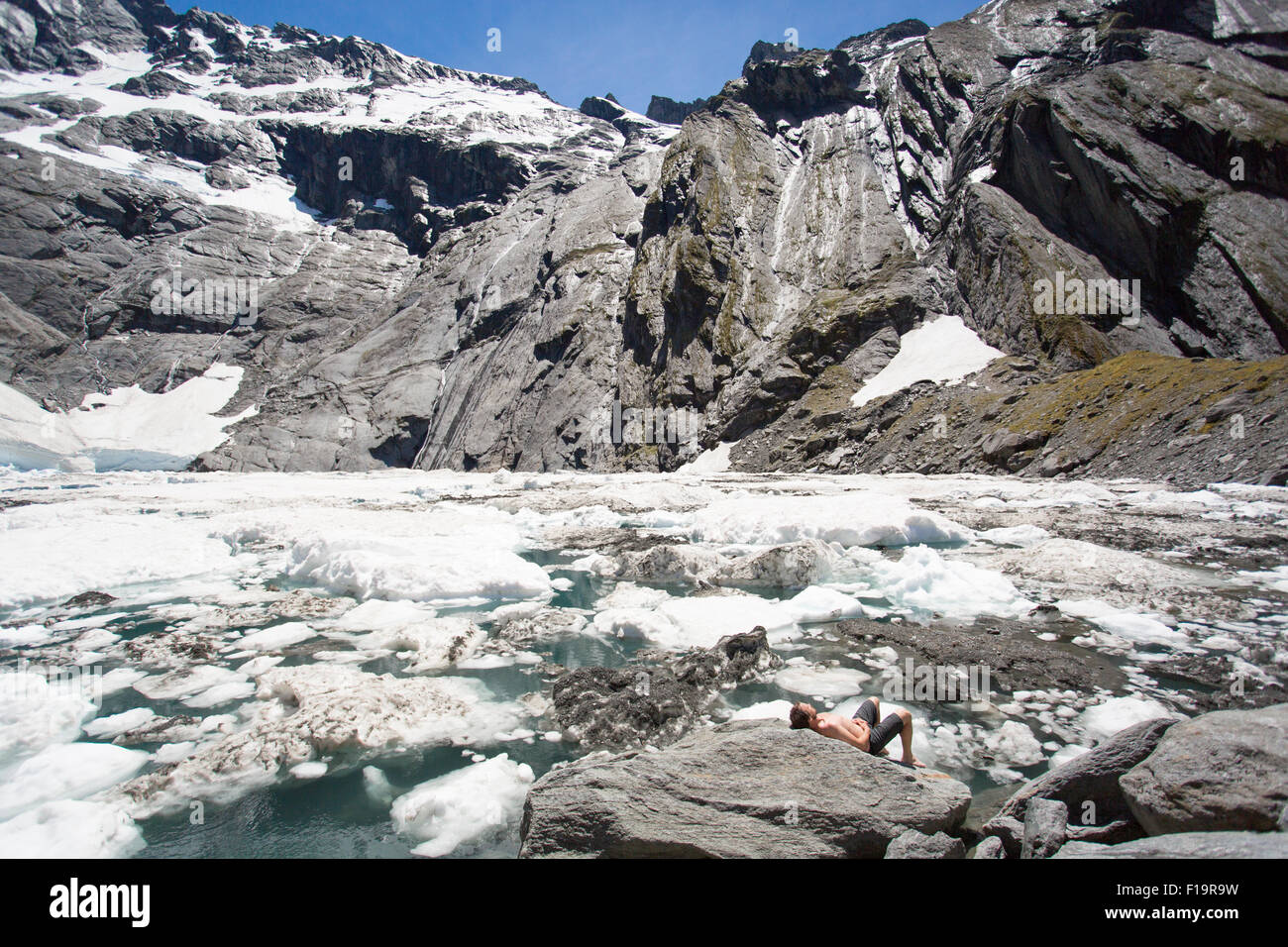 Nuova Zelanda aka Aotearoa, Isola del Sud, Mt Aspiring National Park, Lago crogiolo, turistico a prendere il sole sulla roccia accanto a iceberg. Foto Stock