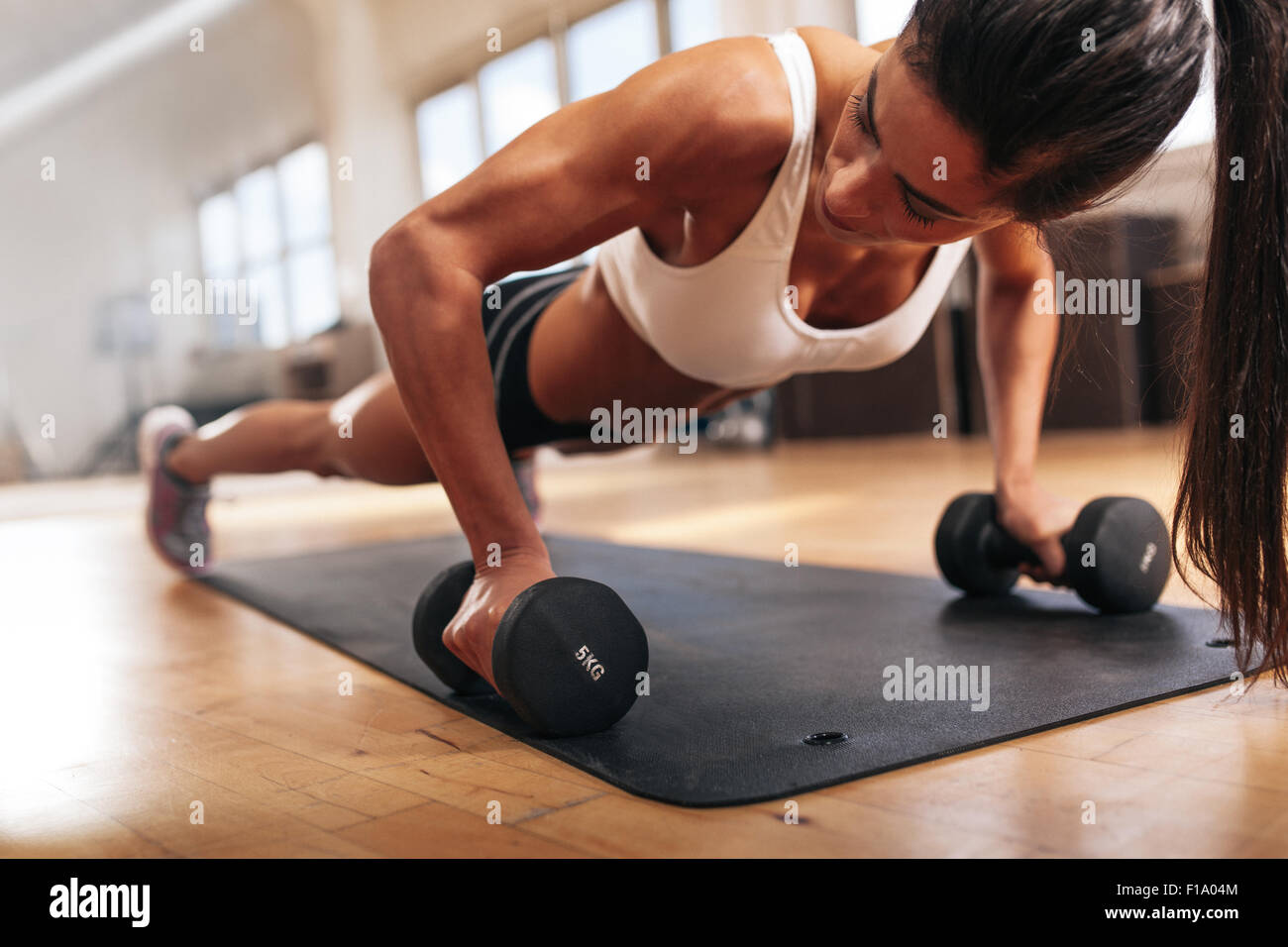 Palestra donna facendo push-up esercizio con il manubrio. Femmina forte facendo crossfit allenamento. Foto Stock