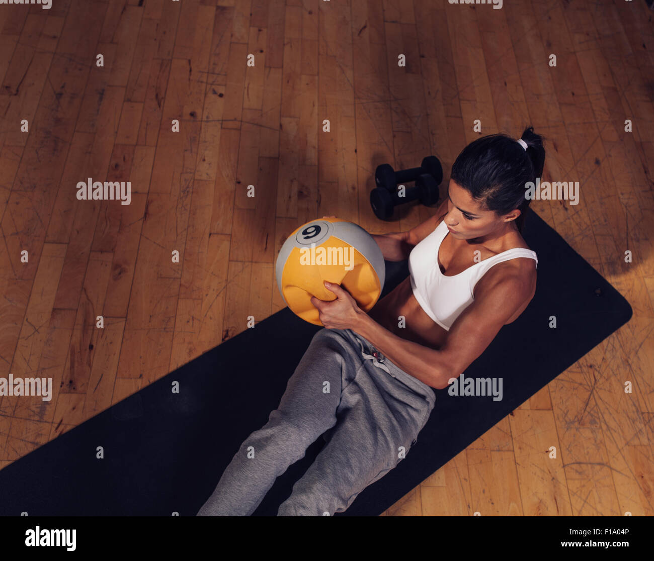 Vista superiore del forte giovane donna facendo allenamento core utilizzando kettlebell peso. Femmina muscolare esercitando sul tappetino fitness in palestra. Foto Stock