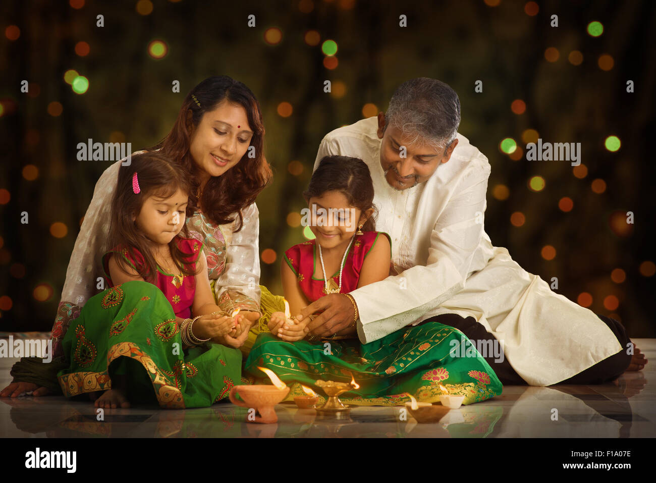 Famiglia indiana nel tradizionale sari illuminazione lampada a olio e celebrare il Diwali o deepavali, fesitval di luci a casa. Bambina Foto Stock
