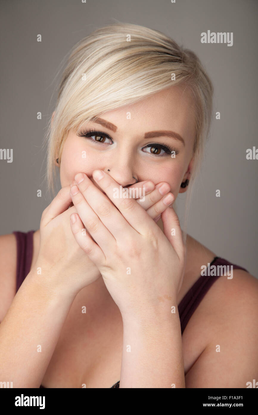 Bella ragazza adolescente ridendo che copre la bocca con entrambe le mani. Foto Stock