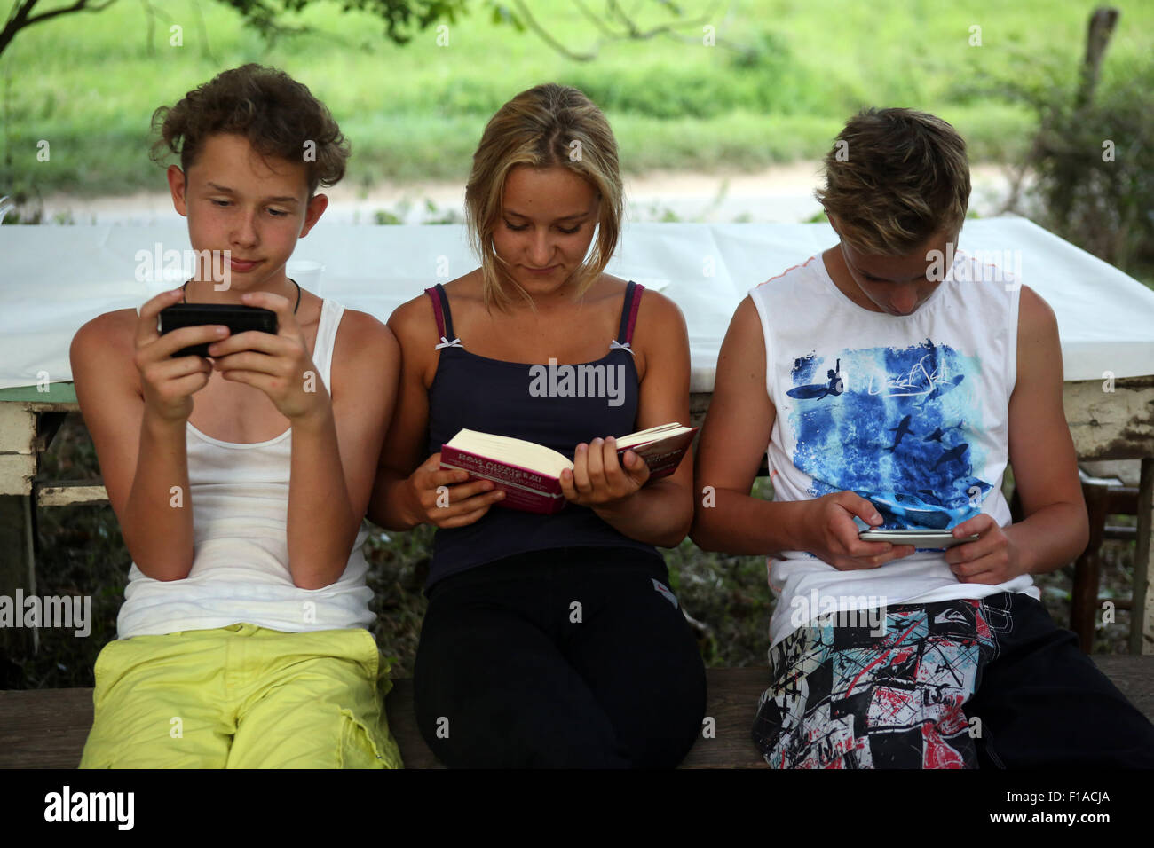 Il lago di Bolsena, Italia, ragazzi giocare con il loro smartphone mentre una ragazza in un libro la lettura Foto Stock