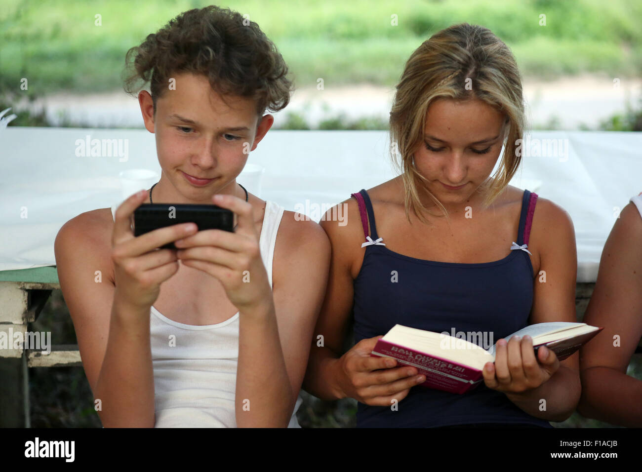Il lago di Bolsena, Italia, ragazzo giocando con il suo smartphone mentre una ragazza in un libro la lettura Foto Stock