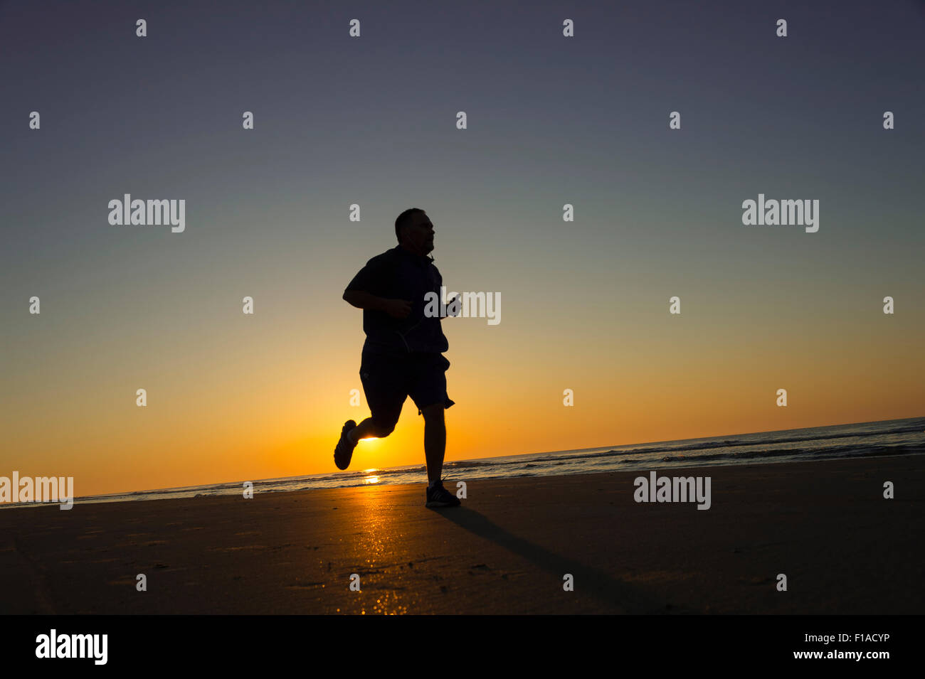 Fat Man in esecuzione sulla spiaggia al tramonto Foto Stock