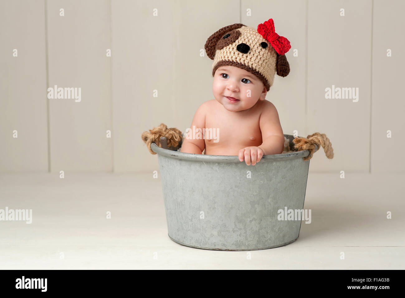 Sei mesi bambina indossa un uncinetto cucciolo di cane Hat. Girato in Studio su un bianco con pavimento in legno e sullo sfondo. Foto Stock