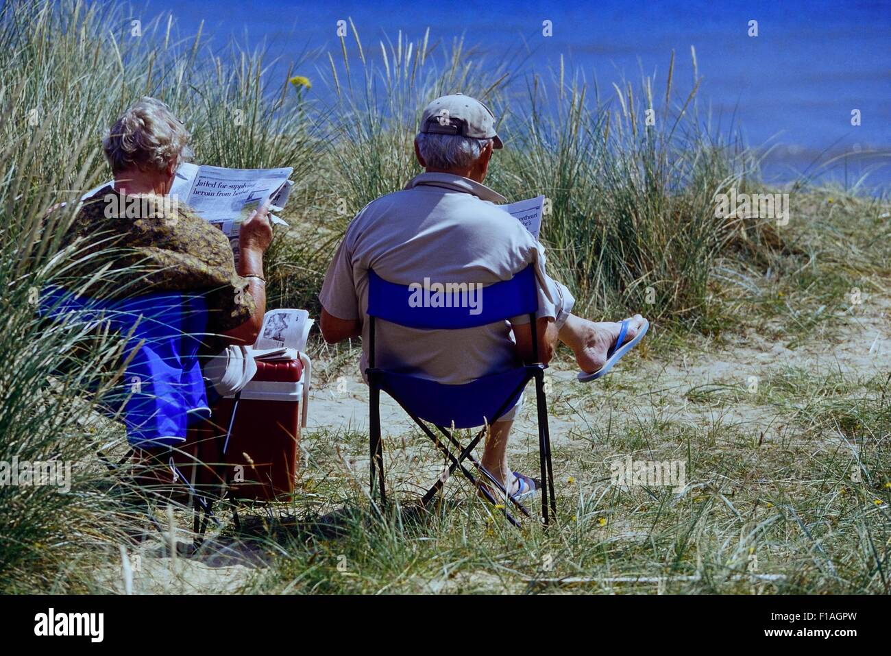 Coppia di anziani seduti su una spiaggia di lettura. In Inghilterra. Regno Unito Foto Stock