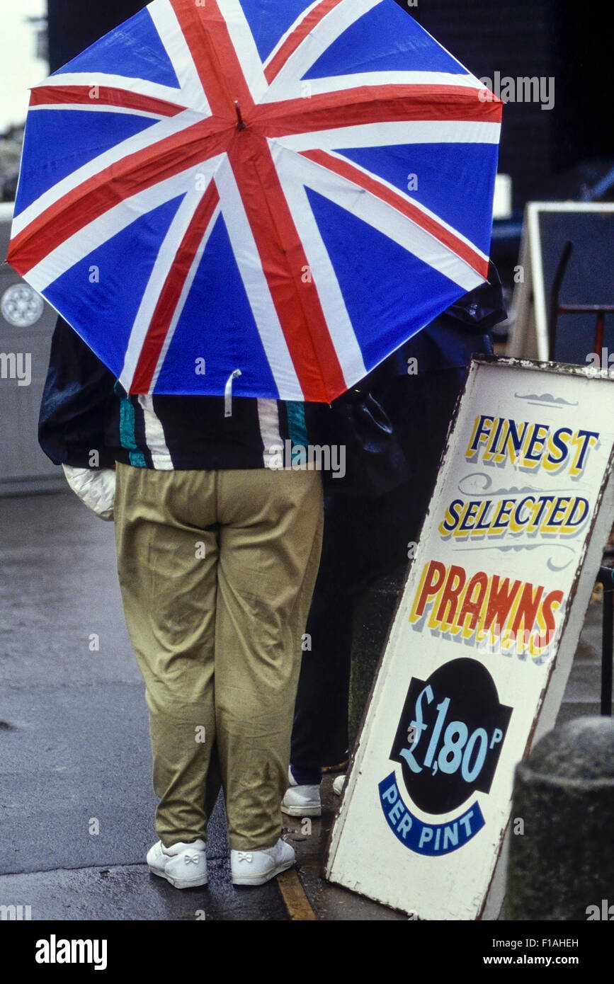 Un turista si ripara dalla pioggia sotto un Unione Jack ombrello. Hastings. East Sussex. In Inghilterra. Regno Unito Foto Stock