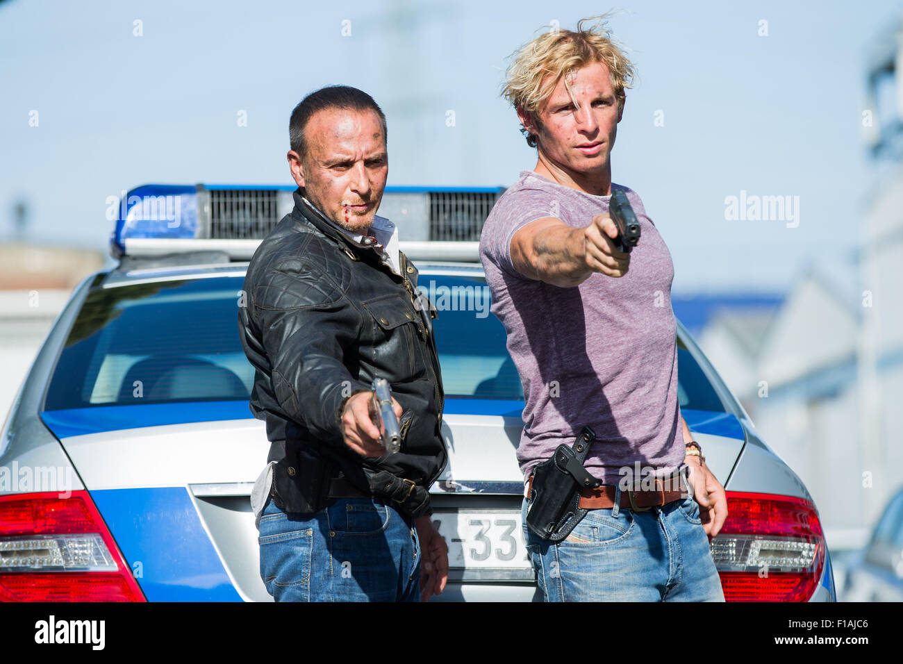 Gli attori Erdogan Atalay (l - come 'Semiro Gerkhan') e Daniel Roesner (come Paolo Renner) pongono con le loro pistole nella parte anteriore di una macchina della polizia sul set di azione RTL TV show 'Allarme fuer Cobra 11' in Huerth, Germania il 31 agosto 2015. Foto: ROLF VENNENBERND/dpa Foto Stock