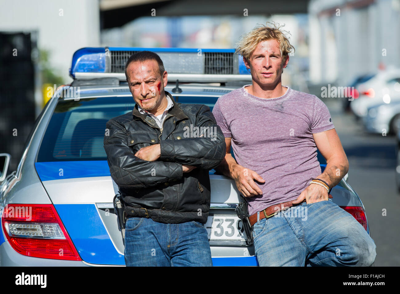 Gli attori Erdogan Atalay (l - come 'Semiro Gerkhan') e Daniel Roesner (come Paolo Renner) pongono con le loro pistole nella parte anteriore di una macchina della polizia sul set di azione RTL TV show 'Allarme fuer Cobra 11' in Huerth, Germania il 31 agosto 2015. Foto: ROLF VENNENBERND/dpa Foto Stock
