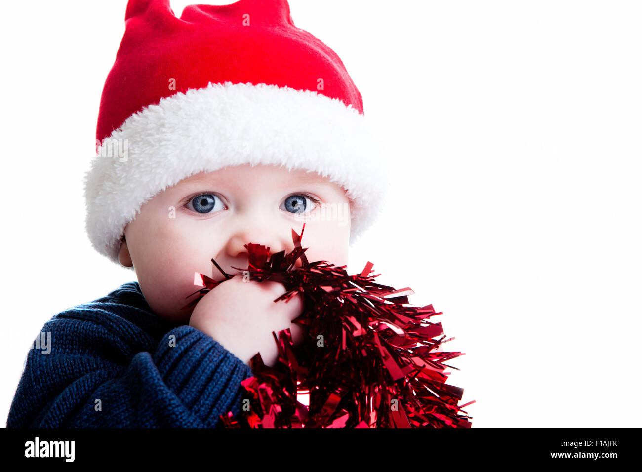 Un studio shot del bambino contro uno sfondo bianco che indossa un cappello di Natale e azienda tinsel Foto Stock