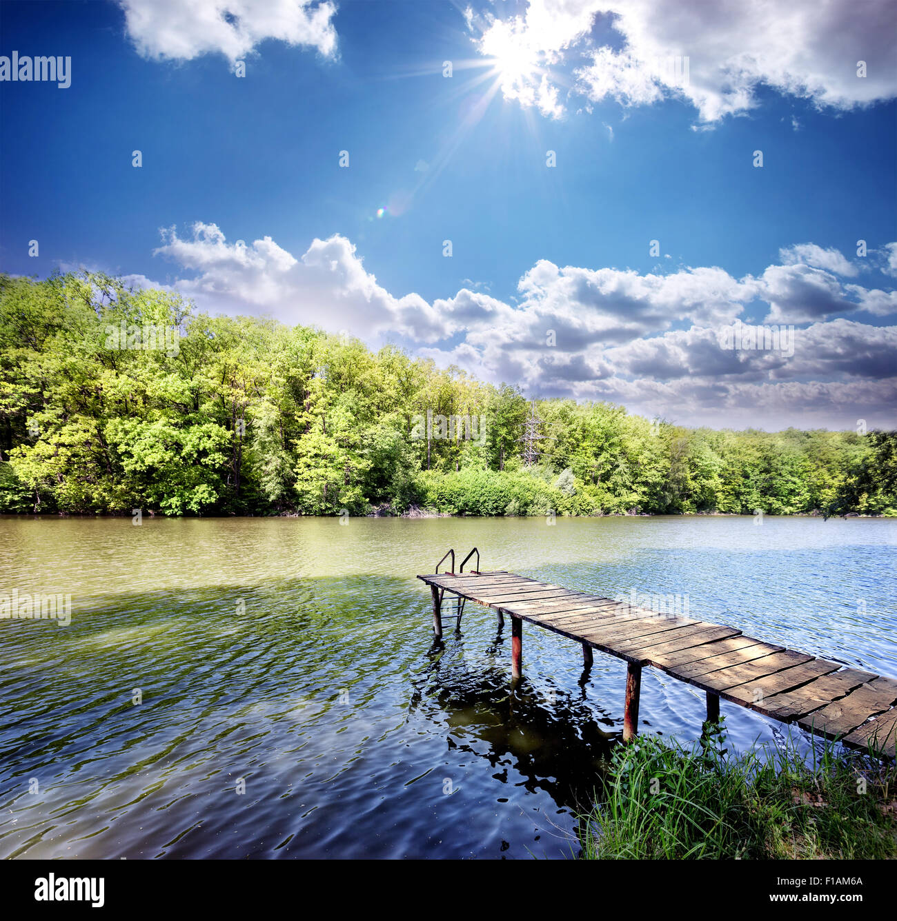 Il molo di legno in un piccolo lago blu sotto il cielo sereno Foto Stock
