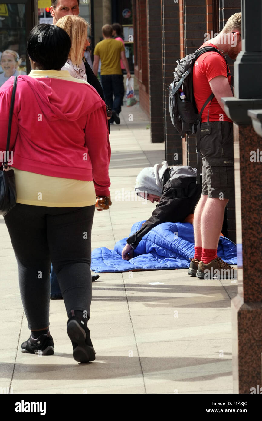 Senzatetto uomo seduto a fianco di un punto di contanti per le strade di Manchester mentre la gente in coda al bancomat. fotografia DON TONGE Foto Stock