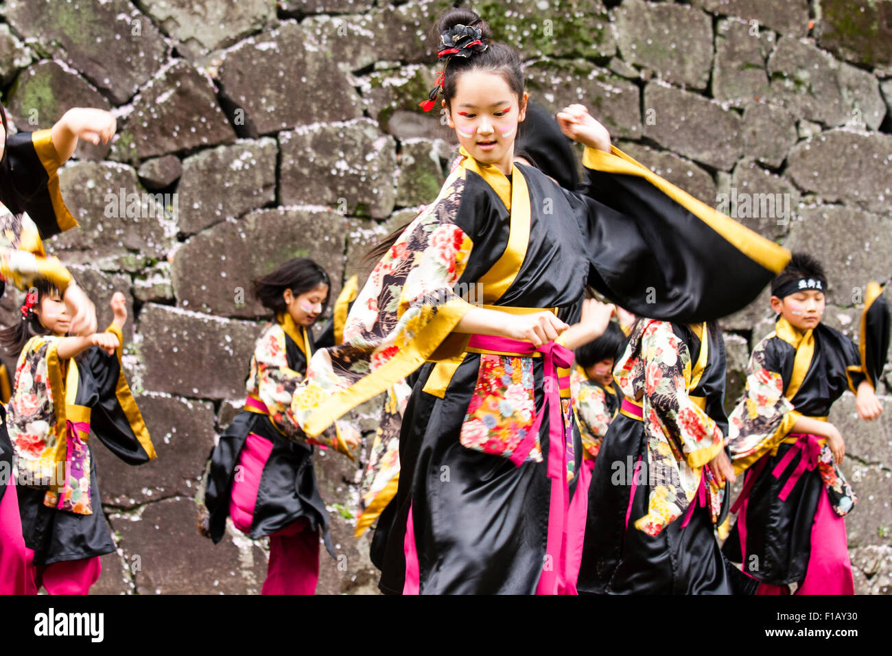 Kumamoto, Giappone, Yosakoi Festival. Corpo di ballo di bambini, 10-16 anni, tenendo naruko e in nero happi coats, ballare nella parte anteriore del muro di castello Foto Stock