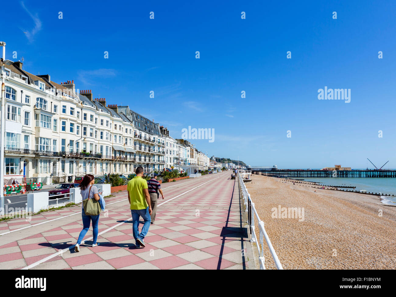 Il lungomare e la spiaggia con la bruciata pier nella distanza, Hastings, East Sussex England, Regno Unito Foto Stock