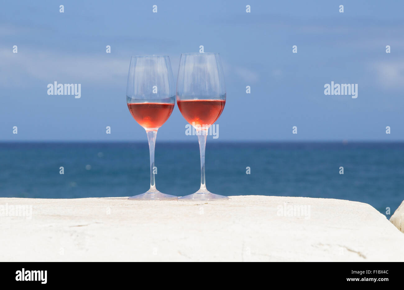 Due bicchieri di vino rosato su una parete dipinta di bianco, blu oceano in background Foto Stock