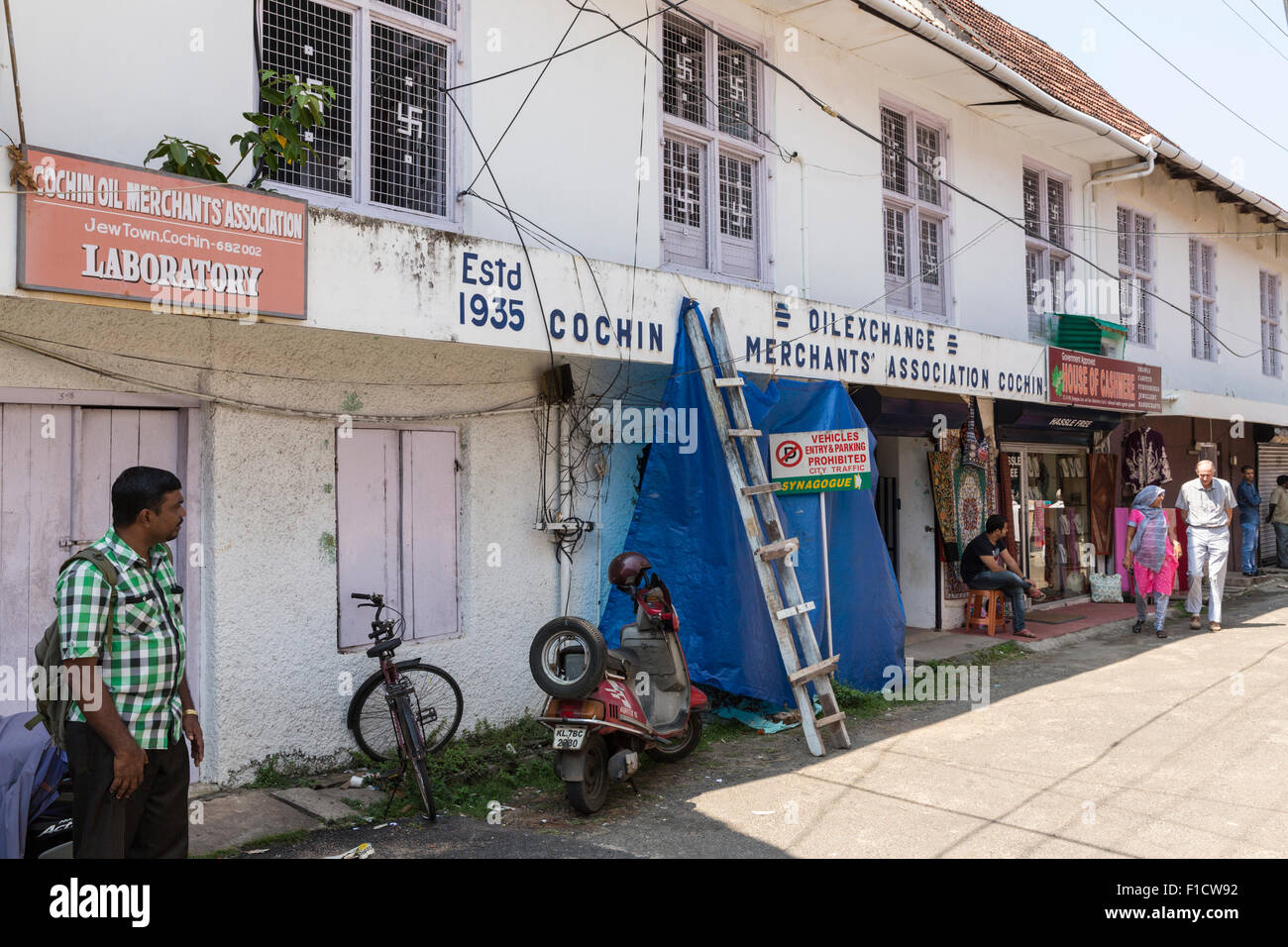 Edificio adibito a magazzino e pedoni in città Giudeo, Kochi, India. Nota Il Hindu svastiche decorare la finestra di griglie Foto Stock