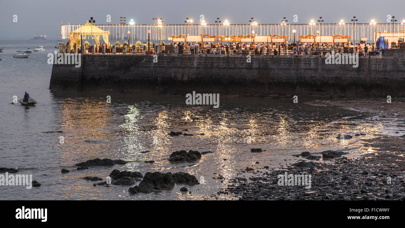 Indiano grande festa di nozze su un molo di pietra che si estende nel porto di Mumbai. Gli ospiti e il personale di stand gastronomici sono illuminati al crepuscolo Foto Stock