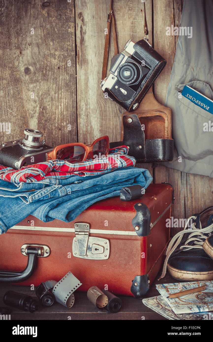 Vecchia valigia viaggio, sneakers, abbigliamento, occhiali da sole, mappe, pellicola e pellicola retrò fotocamera . Vintage stilizzato. Foto Stock