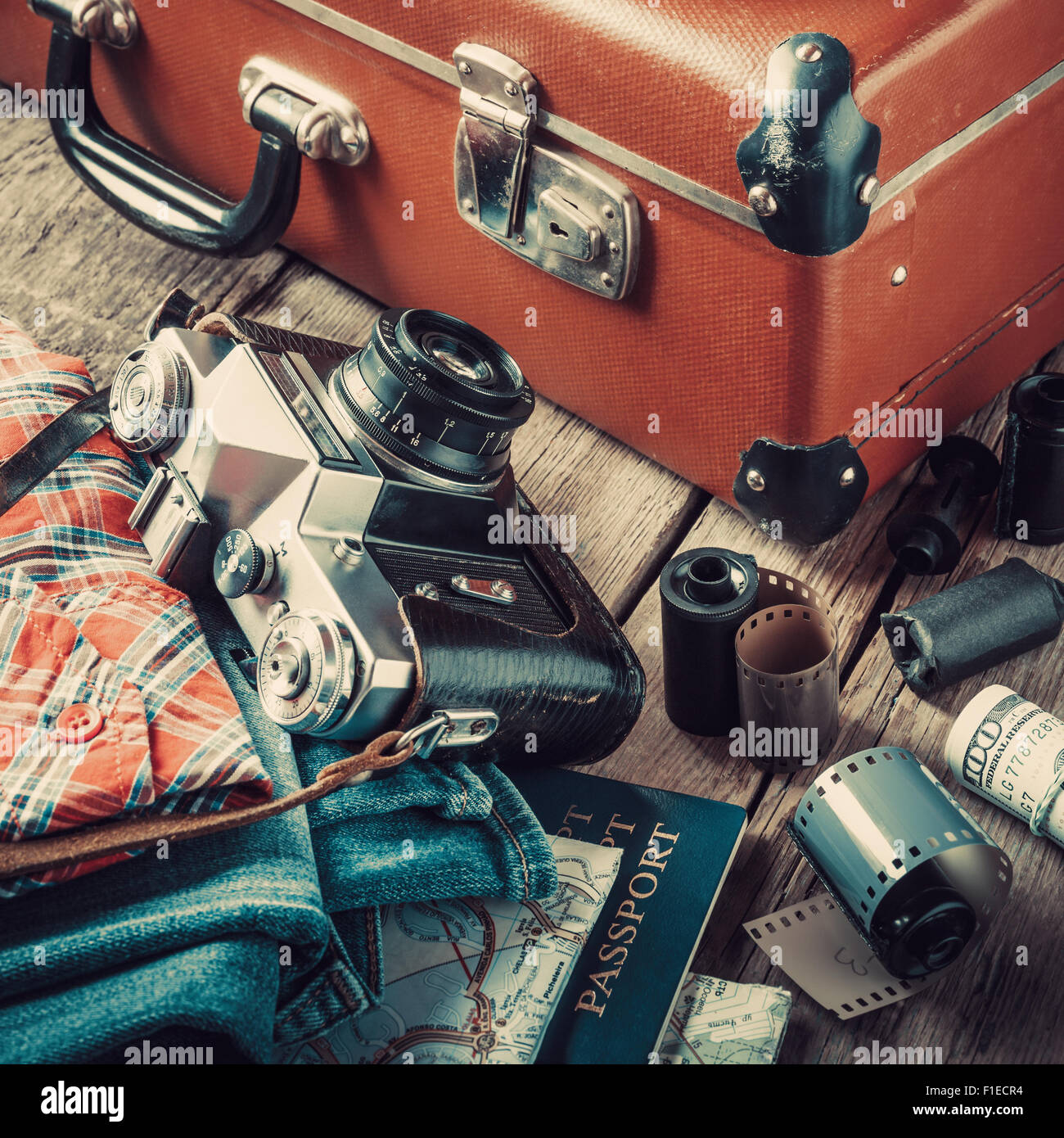 Vecchia valigia viaggio, abbigliamento, mappa, pellicola e pellicola retrò fotocamera su sfondo di legno. Vintage stilizzato. Foto Stock