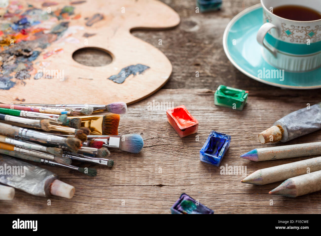 Pennelli, artista tavolozza, matite, tazza di caffè, acquarello e colori a olio sulla scrivania in studio di pittore. Foto Stock