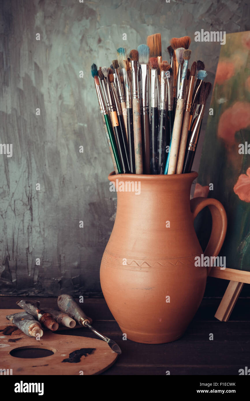 Pennelli in una brocca da potters argilla, palette, tubi di vernice e pittura in studio dell'artista. Foto Stock