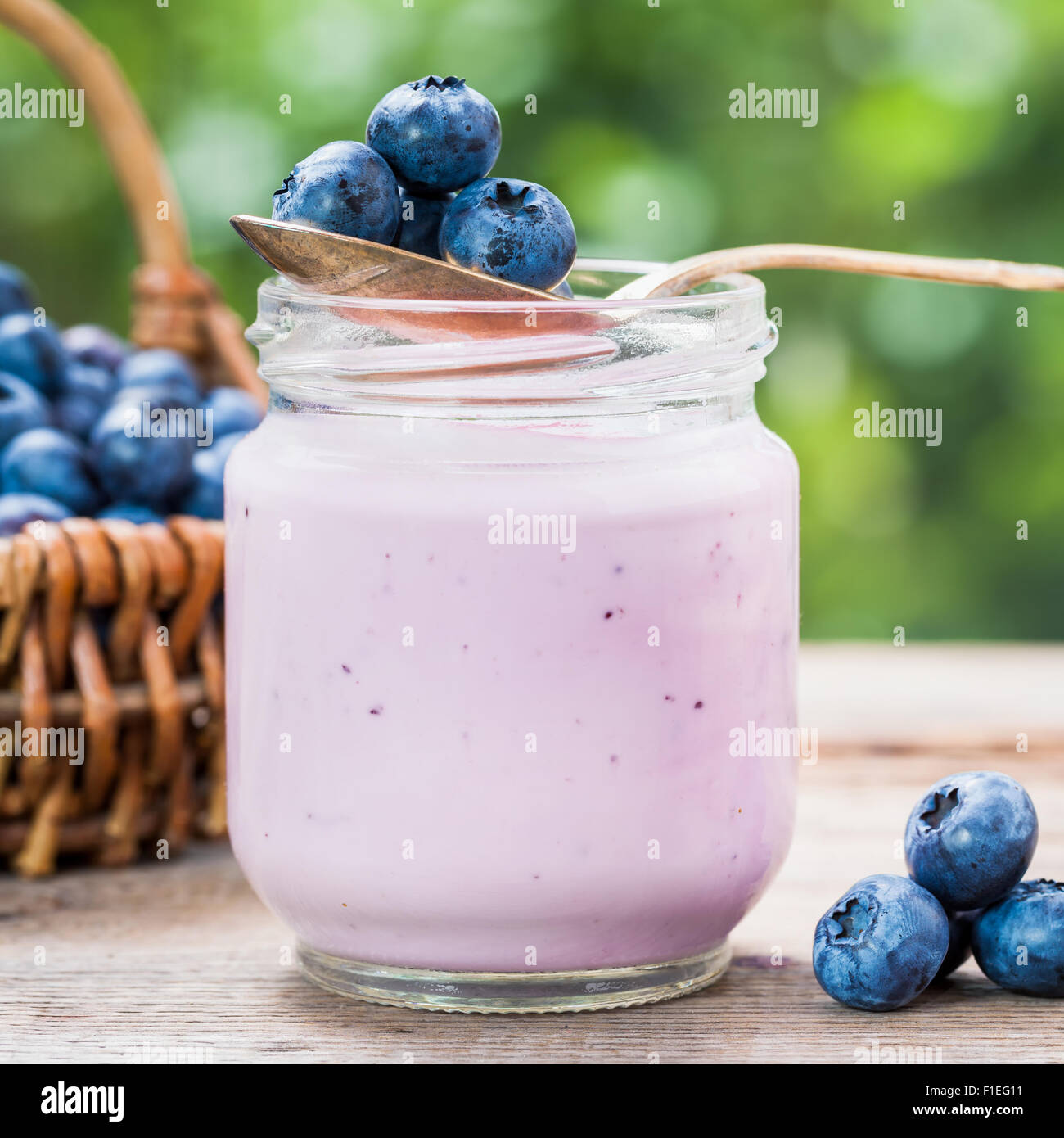 Mirtilli freschi yogurt in un barattolo di vetro e cesto di vimini con mirtilli neri su sfondo. Foto Stock