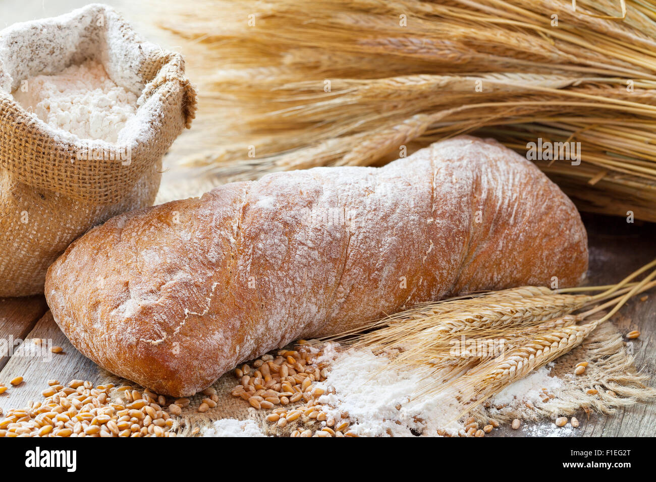 Pane fresco, sacco di farina di frumento e orecchie sul tavolo di legno. Foto Stock