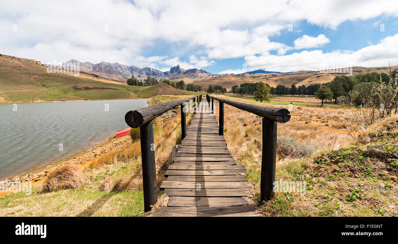 Vista attraverso il ponte pedonale con rosso barca sulla riva del lago e montagne Drakensberg nella distanza Foto Stock