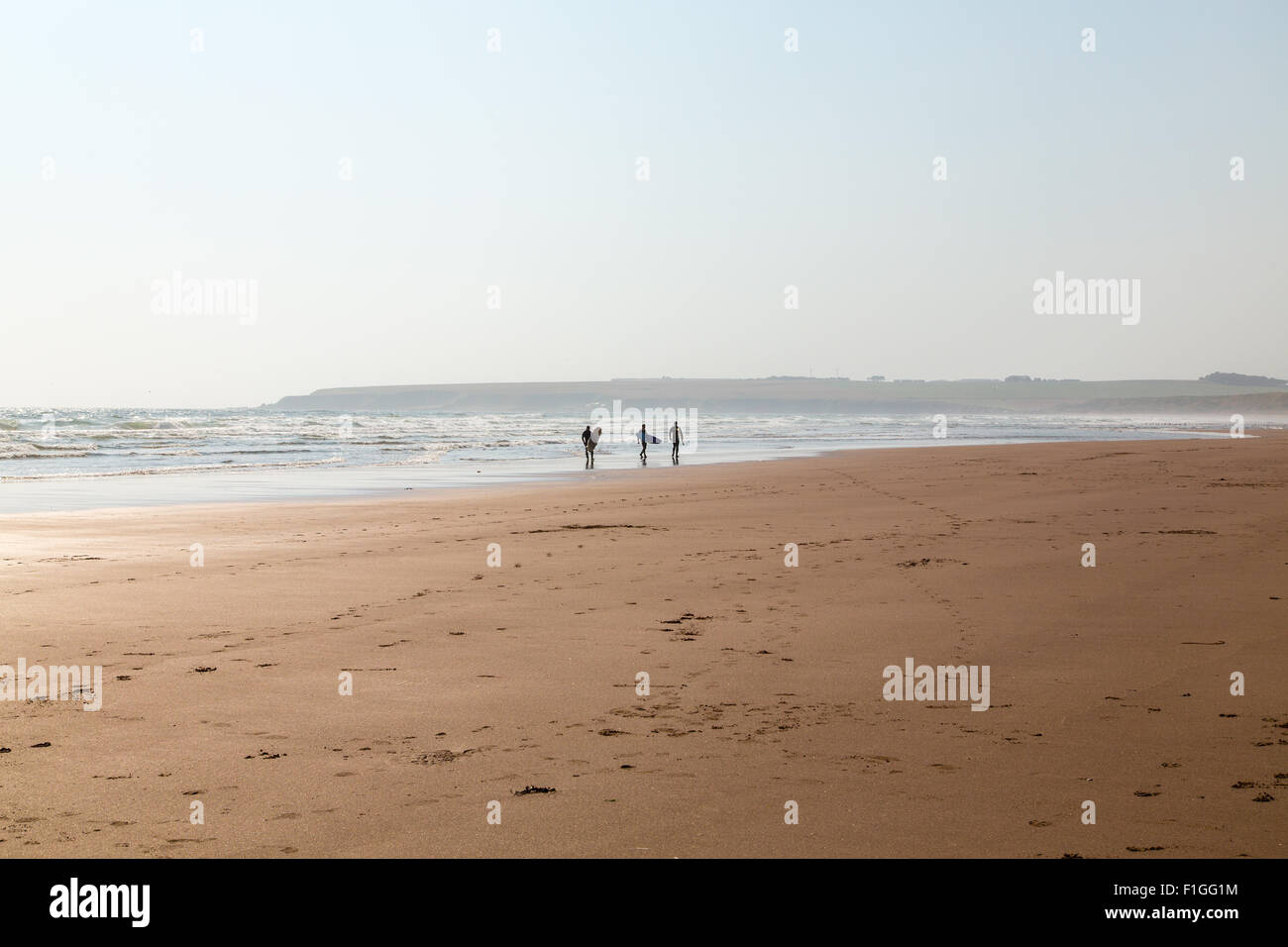 Surfers camminando lungo il bordo delle acque a Lunan Bay Foto Stock