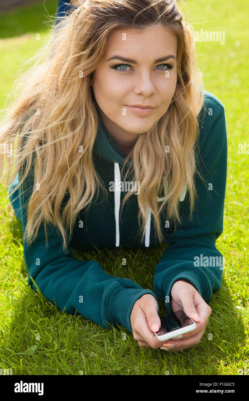 Bella ragazza adolescente sdraiati sull'erba in possesso di un telefono cellulare nelle sue mani. Foto Stock