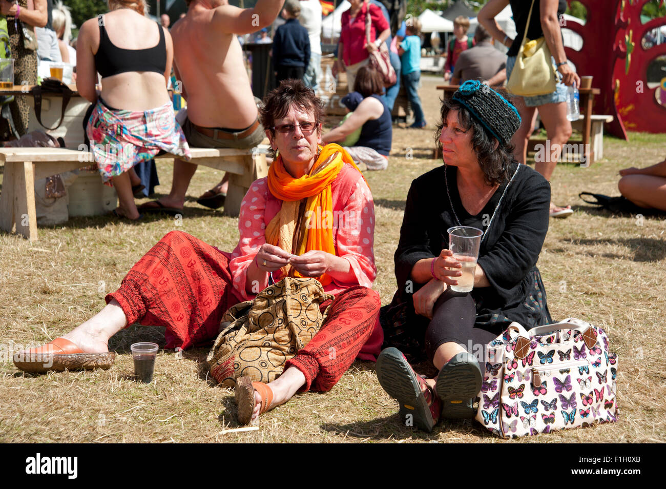 Due donne di mezza età sedersi sull'erba a bere birra in estate il sole al porto Eliot Festival Cornovaglia Foto Stock