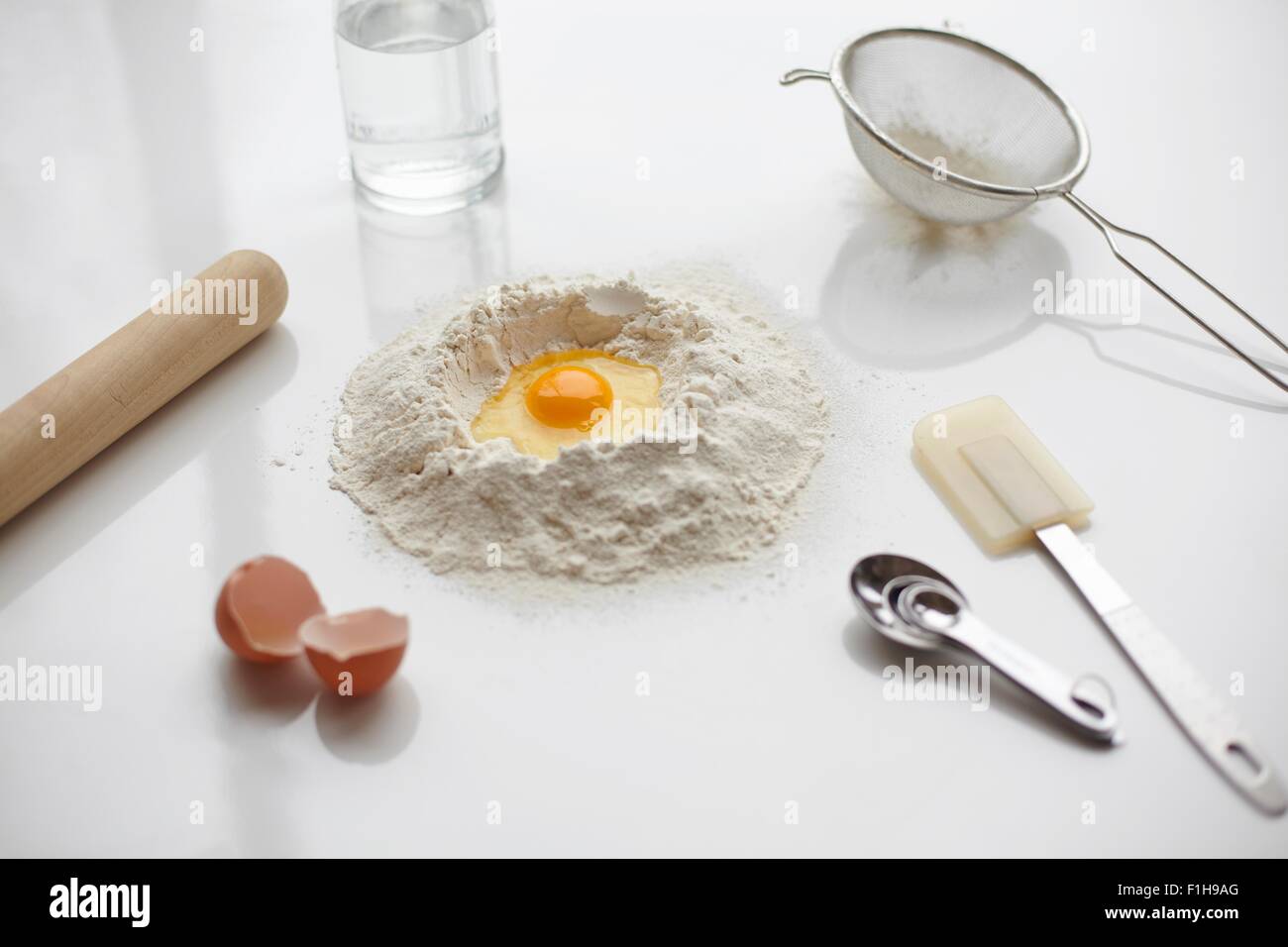 Preparazione di cottura con uovo crudo nel centro della pila di farina e utensili da cucina Foto Stock