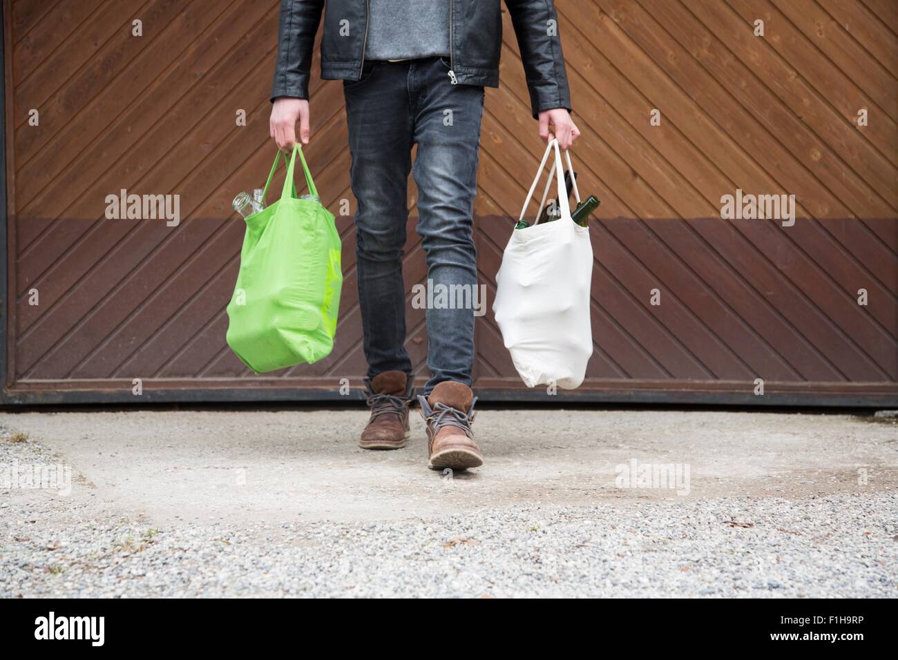 Ragazzo adolescente riutilizzabili trasporto delle borse della spesa pieno di bottiglie vuote per il riciclaggio Foto Stock